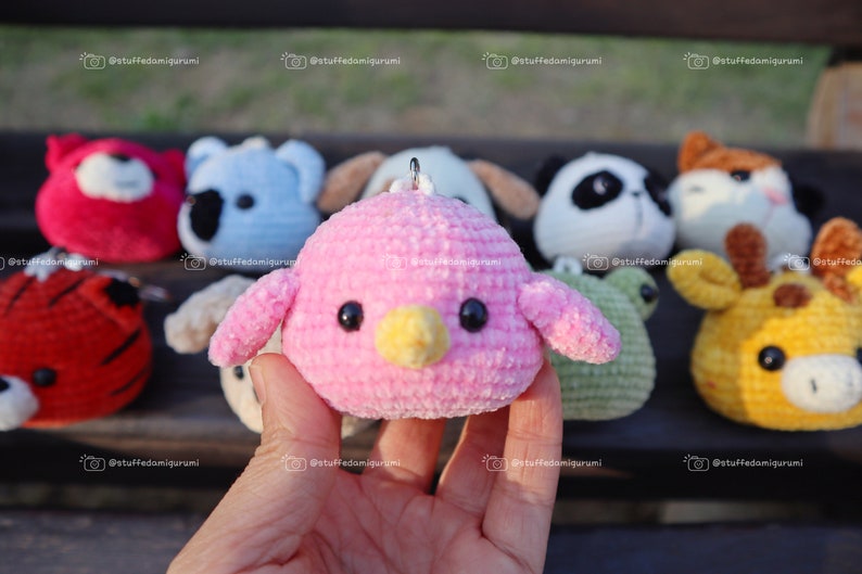 May include: A collection of crocheted animal plushies, including a pink bird, a red tiger, a blue koala, a white panda, a brown dog, a green frog, a yellow giraffe, and a brown fox. The plushies are all small and have cute faces.