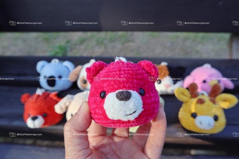 May include: A collection of small crocheted stuffed animals, including a pink bear, a blue koala, a brown dog, a black and white cat, a pink pig, and a yellow giraffe. The animals are all holding a small key chain.