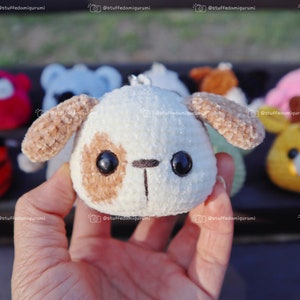 May include: A close-up of a small, white plush dog with brown ears and spots. The dog has large black eyes and a small black nose. The dog is being held in a hand.