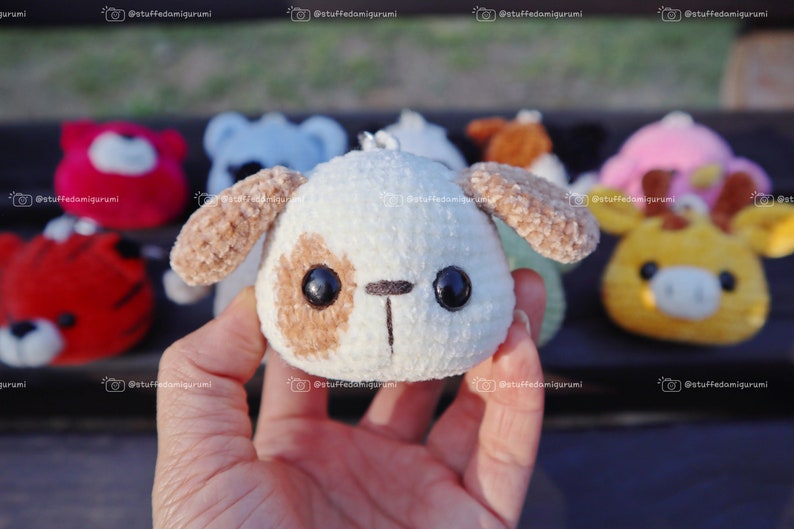 May include: A close-up of a small, white plush dog with brown ears and spots. The dog has large black eyes and a small black nose. The dog is being held in a hand.