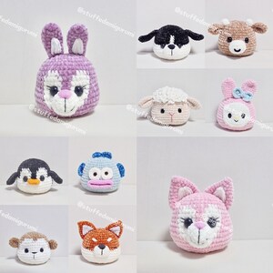 May include: A collection of handmade crocheted animal head plushies. The plushies are made in a variety of colors and styles, including a pink bunny, a blue monkey, a white sheep, a brown cow, a pink cat, a white penguin, a brown fox, and a white monkey.