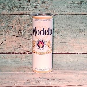 May include: A white Modelo-branded tumbler with a clear lid. The tumbler features the Modelo logo in black, gold, and red, along with the words "IMPORTED BEER" and "CERVECERIA MODELO MEXICO 1925". The tumbler is cylindrical and appears to be made of stainless steel.