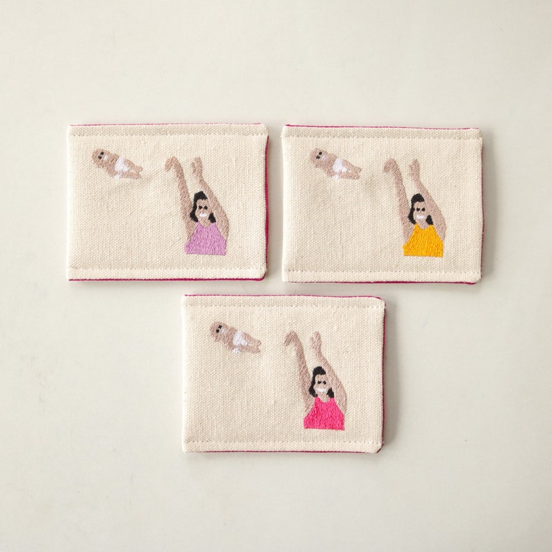 Puede incluir: Tres tarjetas de lona bordadas con detalles en rosa, amarillo y rojo. Cada tarjeta muestra a una mujer lanzando un beb&eacute; al aire.
