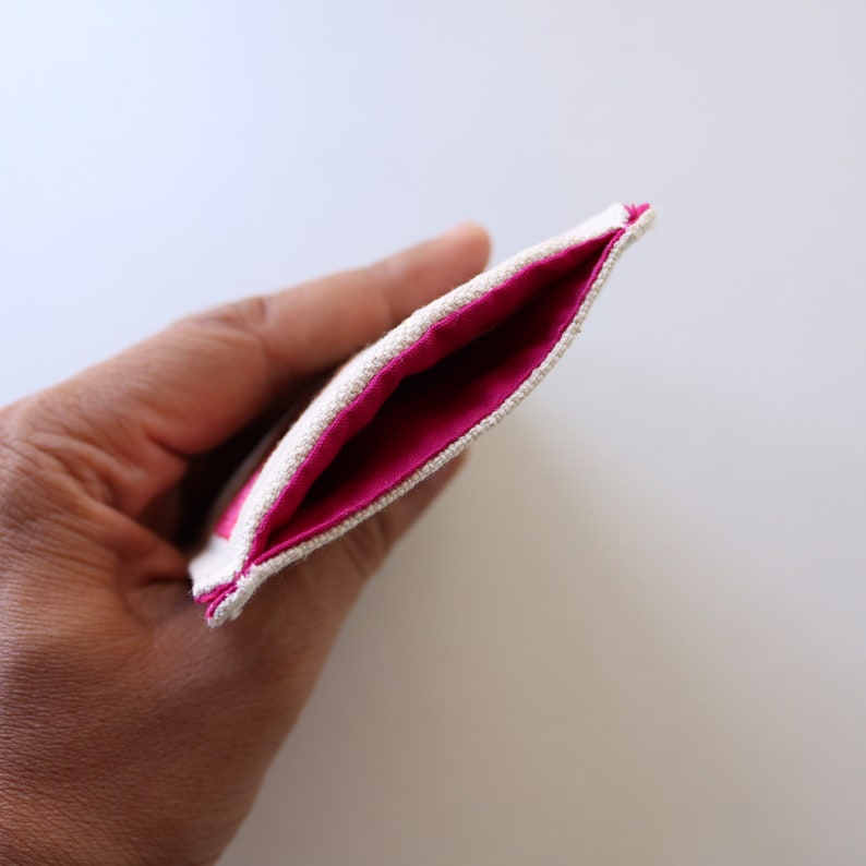Puede incluir: Una peque&ntilde;a bolsa hecha de tela beige con un forro rosa. La bolsa est&aacute; abierta y el forro es visible.