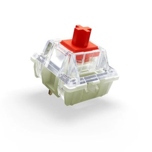 May include: A clear mechanical keyboard switch with a red keycap. The switch has a cross-shaped stem and a transparent housing.