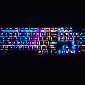 May include: A black keyboard with colorful backlighting. The keys have various symbols and letters, including the Star Wars logo and other characters. The keyboard is lit up in a variety of colors, including blue, green, purple, and red.