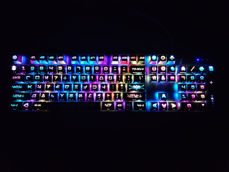 May include: A black keyboard with colorful backlighting. The keys have various symbols and letters, including the Star Wars logo and other characters. The keyboard is lit up in a variety of colors, including blue, green, purple, and red.