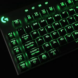 May include: A backlit gaming keyboard with green illumination. The keys are black with green lettering and symbols. The keyboard has a 'G' logo and special keys with gaming icons. The word 'HALO' is visible on the keyboard.