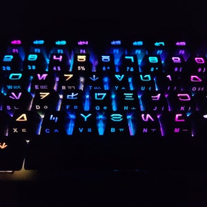 May include: A black keyboard with colorful backlighting. The keys are labeled with letters, numbers, and symbols. The backlighting is in shades of blue, purple, and pink.