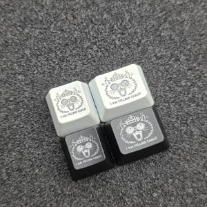 May include: Four square mechanical keyboard keycaps in white and black. Each keycap features a graphic of a cat wearing a crown and glasses with its mouth open, accompanied by the printed text "I AM YELLING CARL!!!" in a clear, sans-serif font.