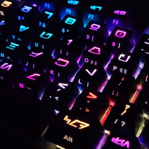May include: A close-up of a black keyboard with colorful backlighting. The keys are arranged in a hexagonal pattern and feature various symbols and letters. The keyboard is lit with a rainbow of colors, including red, orange, yellow, green, blue, indigo, and violet.