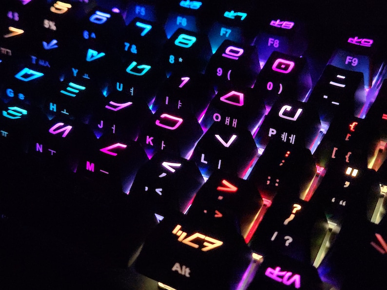 May include: A close-up of a black keyboard with colorful backlighting. The keys are arranged in a hexagonal pattern and feature various symbols and letters. The keyboard is lit with a rainbow of colors, including red, orange, yellow, green, blue, indigo, and violet.
