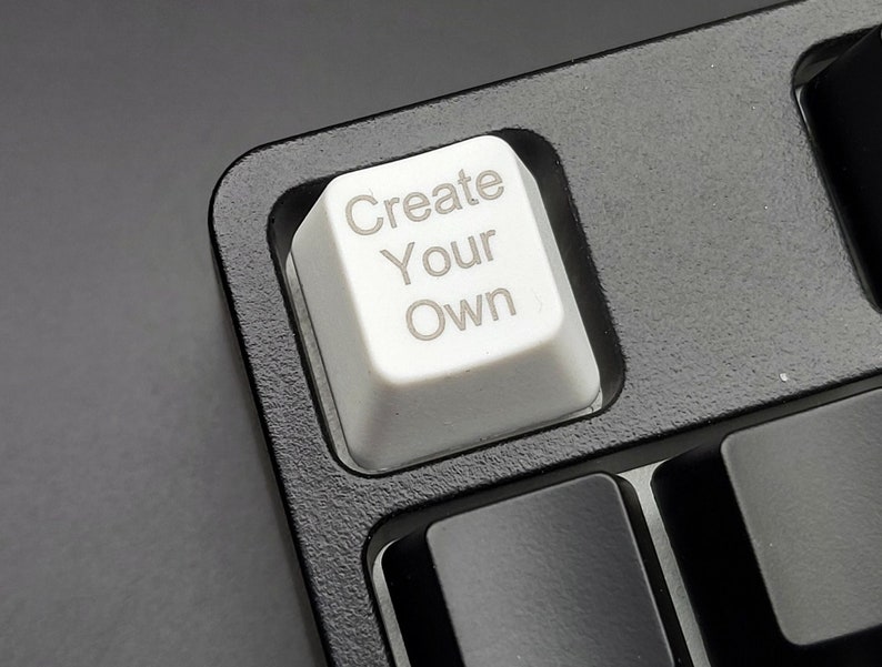 Może przedstawiać: Biały klawisz klawiatury z nadrukiem "Create Your Own". Klawisz znajduje się na czarnej klawiaturze.