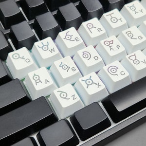 Op de afbeelding: Wit toetsenbord met zwarte toetsen en aangepaste toetsen met verschillende symbolen en letters. De toetsen hebben een witte achtergrond met grijze symbolen en letters.