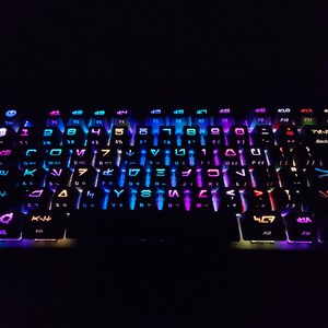 May include: A black keyboard with rainbow colored keys. The keys have various symbols and letters on them, including the letters "F1" through "F12" and the words "Backspace", "Enter", and "Shift".