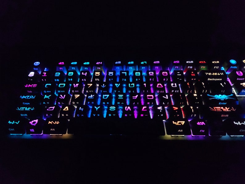May include: A black keyboard with rainbow colored keys. The keys have various symbols and letters on them, including the letters "F1" through "F12" and the words "Backspace", "Enter", and "Shift".