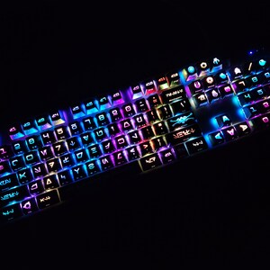 May include: A black mechanical keyboard with colorful backlighting. The keys have various symbols and letters, including numbers, arrows, and special characters. The keyboard has a white frame and a black base.