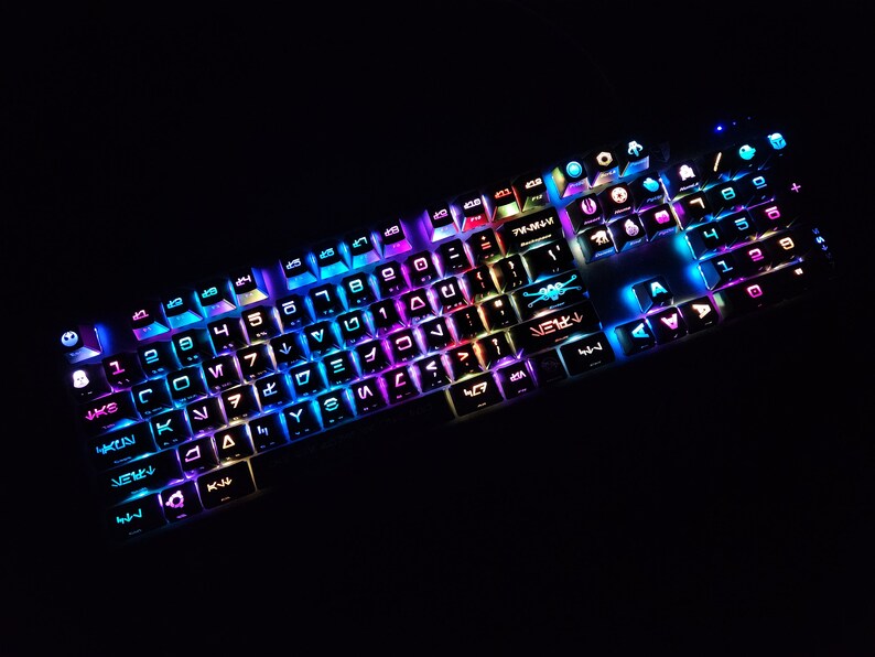 May include: A black mechanical keyboard with colorful backlighting. The keys have various symbols and letters, including numbers, arrows, and special characters. The keyboard has a white frame and a black base.