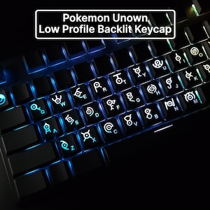 Könnte beinhalten: Schwarze Tastatur mit blau beleuchteten Tasten. Die Tastenkappen zeigen weiße Pokemon Unown-Symbole. Oben auf der Tastatur steht der Text "Pokemon Unown, Low Profile Backlit Keycap" in einem weißen Rechteck.