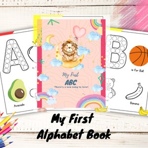 May include: A colorful alphabet book for children with illustrations of an avocado, a basketball, a banana, and a lion. The book has a pink cover with the title "My First ABC" and the text "There's a new baby to love!"
