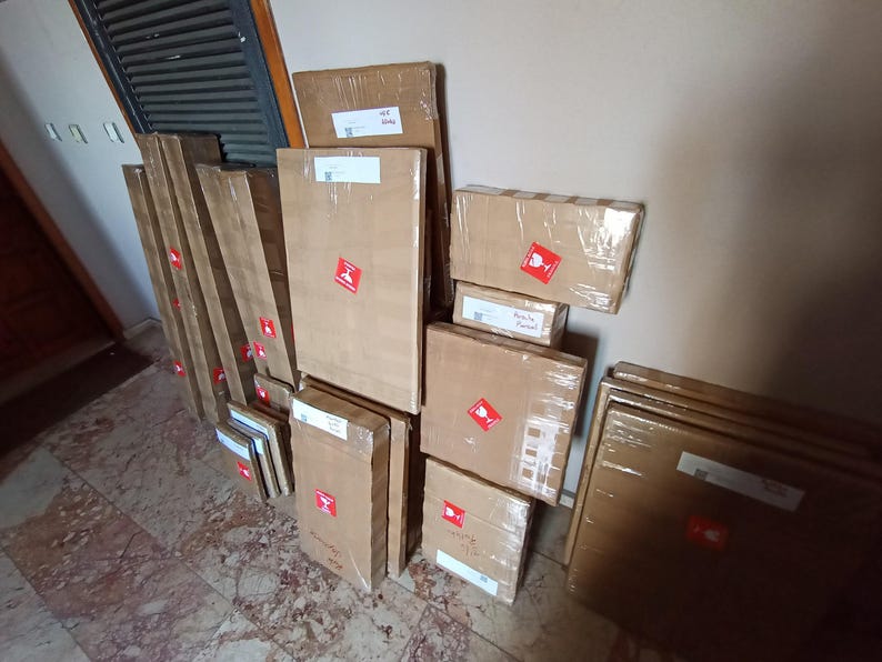 A collection of cardboard boxes and packages wrapped in brown paper, with red shipping labels, stacked against a wall.