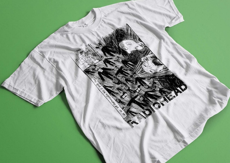 Puede incluir: Camiseta blanca con un estampado gr&aacute;fico en blanco y negro de una imagen de estilo c&oacute;mic. El texto "Radiohead" est&aacute; impreso en negro en la parte inferior de la imagen.