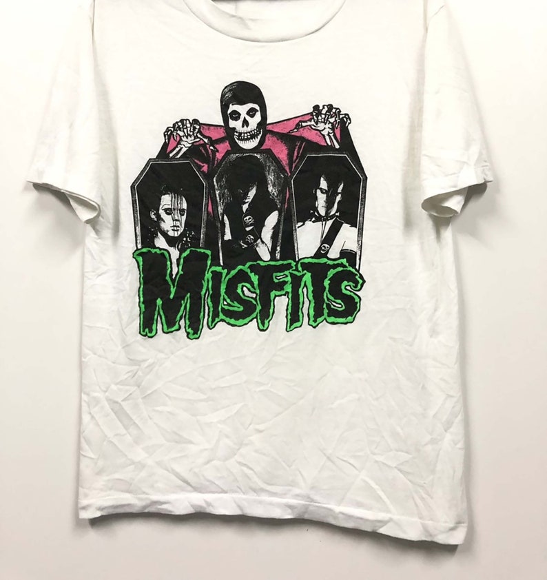 May include: White t-shirt with a black and white graphic of the band Misfits. The graphic features the band members in coffins with a skull-faced figure holding up a pink sheet.