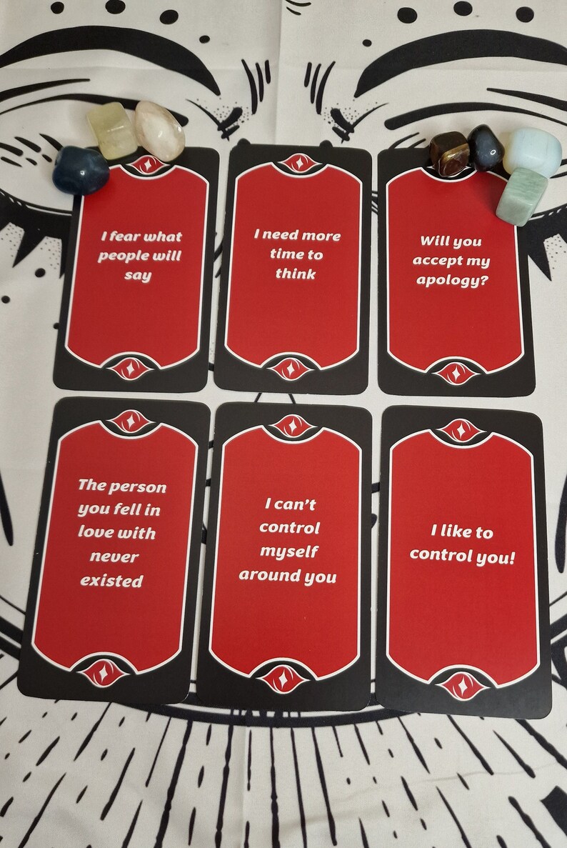 Puede incluir: Seis cartas de tarot con caras rojas y bordes negros, cada una con texto blanco. Las frases incluyen "Temo lo que dir&aacute; la gente" y "&iexcl;Me gusta controlarte!". Varias piedras preciosas se colocan cerca de las cartas.