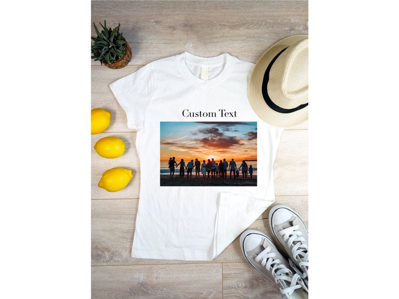 Puede incluir: Camiseta blanca con una foto de un grupo de personas silueteados contra una puesta de sol en una playa. El texto "Custom Text" est&aacute; por encima de la foto.