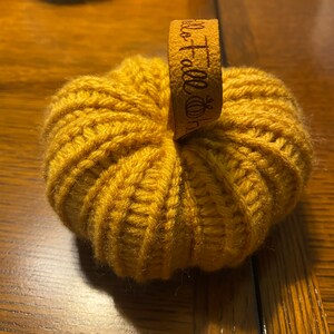 May include: A crocheted pumpkin in a mustard yellow color with a brown leather tag that says "Hello Fall".