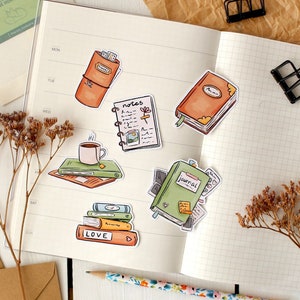 May include: A set of six illustrated stickers featuring various stationery items, including a journal, a notebook, a cup of coffee, a stack of books, and a closed book. The stickers are on a white background with a grid pattern.