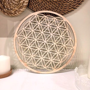 Può includere: Un arazzo da parete in legno con un design geometrico, noto come Fiore della Vita, di colore marrone chiaro.