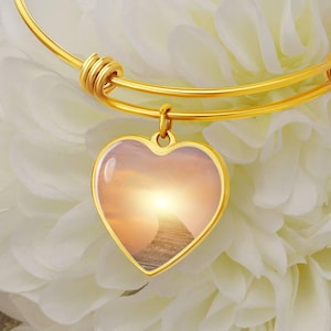 May include: Gold bangle bracelet with a heart-shaped charm featuring a photo of a stairway leading to a bright light in the sky.