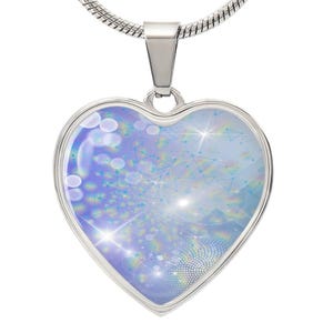 Op de afbeelding: Een zilveren hartvormige ketting met een blauw en wit abstract ontwerp. Het ontwerp heeft een draaiende patroon van lichtblauw, wit en regenboogkleuren.