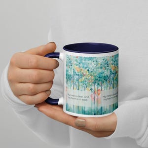 Könnte beinhalten: Weiße Keramik-Kaffeetasse mit dunkelblauem Rand und Henkel. Die Tasse zeigt ein Aquarelldesign eines Waldes mit dem Text "My mind is clear, and my heart is at ease."