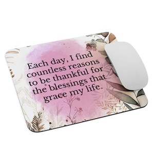 Puede incluir: Alfombrilla de ratón rectangular con diseño floral y el texto "Cada día, encuentro innumerables razones para agradecer las bendiciones que iluminan mi vida." Un ratón de ordenador blanco está a la derecha.