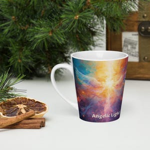 May include: White ceramic coffee mug with a colorful design of an angel with outstretched wings. The mug features a vibrant mix of blues, yellows, and purples, with the words "Angelic Light" printed on the side.