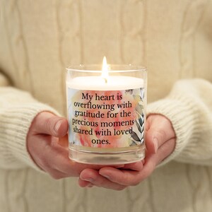May include: A white candle in a clear glass jar with a floral design and the text "My heart is overflowing with gratitude for the precious moments shared with loved ones."