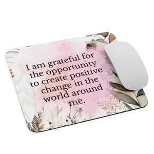 Peut inclure: Un tapis de souris rose et marron avec un motif floral aquarelle et la citation "Je suis reconnaissant pour l'opportunité de créer un changement positif dans le monde qui m'entoure."