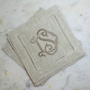 May include: A set of four linen napkins with a brown embroidered monogram of the letter "S" in a decorative script font.