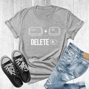 Puede incluir: Camiseta gris con un gráfico blanco de teclas de teclado de computadora que dicen "Ctrl + Alt Supr" con una flecha blanca apuntando hacia la derecha.