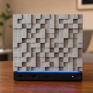 May include: A square acoustic panel featuring a grid of light grey, protruding square blocks of varying depths. The panel sits atop a black rectangular base with a glowing blue light strip, two USB ports, a small slot, and a circular power button.