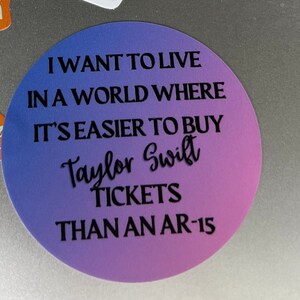 K&ouml;nnte beinhalten: Ein runder Aufkleber mit einem lila und blauen Farbverlauf und dem Text "Ich m&ouml;chte in einer Welt leben, in der es einfacher ist, Taylor Swift Tickets zu kaufen als AR-15."