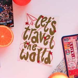 May include: A travel-themed still life featuring a postcard with the text "Let's travel the world", a passport, a Paris souvenir tray, and orange slices. The postcard has a red paper airplane and stars.