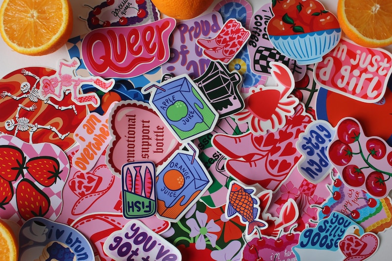 Puede incluir: Una colecci&oacute;n de pegatinas coloridas con varios dise&ntilde;os, que incluyen un esqueleto, un coraz&oacute;n con el texto "botella de apoyo emocional", un pez en una lata, un cangrejo, una caja de jugo, un par de zapatos rosas, una rama de cerezas y la palabra "queer" en letras rosas y rojas.