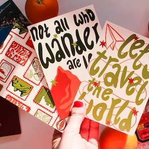 May include: A collection of travel-themed postcards with phrases like "Not all who wander are lost" and "Let's travel the world." The postcards are accompanied by a passport, a map, and an orange slice, suggesting a theme of travel and adventure.