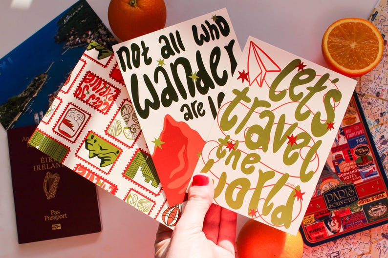 May include: A collection of travel-themed postcards with phrases like "Not all who wander are lost" and "Let's travel the world." The postcards are accompanied by a passport, a map, and an orange slice, suggesting a theme of travel and adventure.