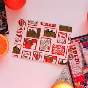 May include: A travel-themed flat lay featuring a patterned passport cover with stamps, a Paris souvenir, a map, and orange slices. The passport cover has the text "Let's go explore".