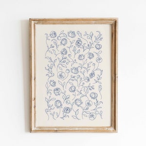 May include: A framed print with a white background and a blue floral pattern. The flowers are drawn in a simple line style and are arranged in a random pattern.