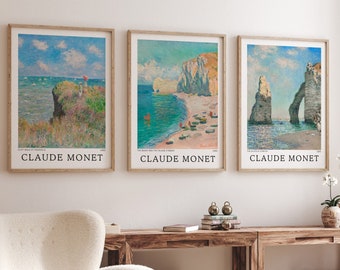 Puede incluir: Tres impresiones de arte enmarcadas de paisajes marinos de Claude Monet. Las impresiones están en un marco de madera claro y presentan un cielo azul, nubes blancas y una playa con acantilados. Las impresiones están colgadas en una pared blanca.